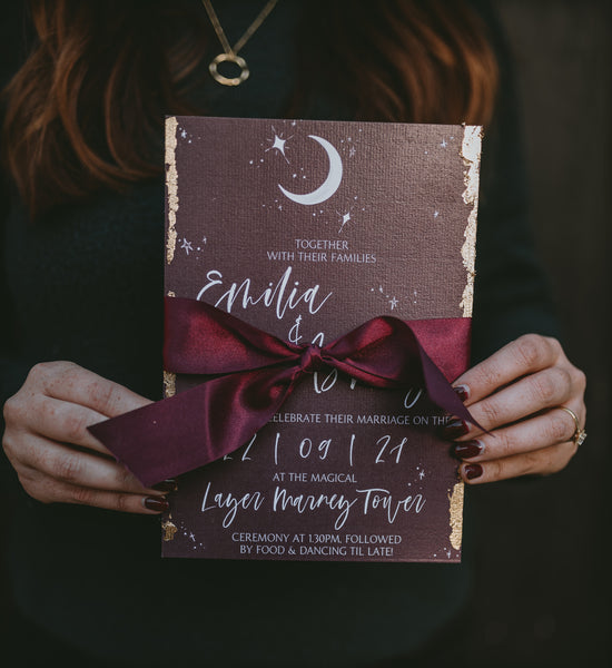 Burgundy moon and star wedding invitation edged in gold leaf with a matching berry coloured silk ribbon